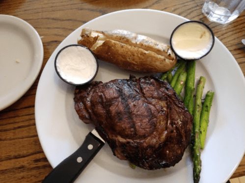 A plate with a grilled steak, baked potato with sour cream, and asparagus on a wooden table.