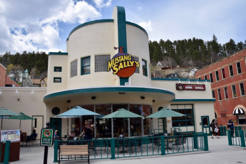 Exterior of Mustang Sally's bar and grill, featuring a round building with green accents and outdoor seating.