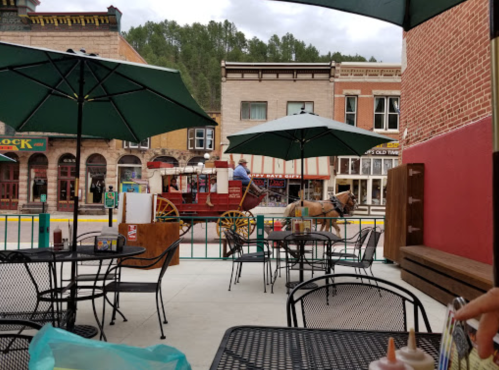 A horse-drawn carriage passes by a café with outdoor seating and umbrellas in a historic town.