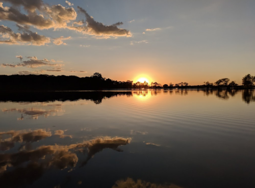 A serene sunset over a calm lake, with vibrant colors reflecting on the water's surface and clouds in the sky.