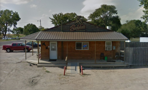 A rustic wooden restaurant with a porch, sign reading "Blackjack Roadhouse," surrounded by trees and parked vehicles.