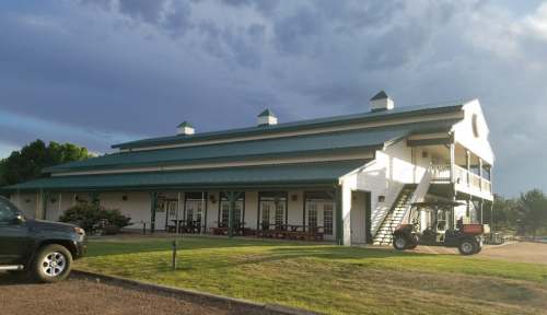 A two-story building with a green metal roof, surrounded by grass and a black vehicle parked nearby.