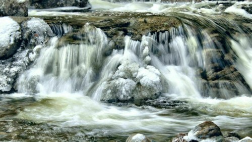 A serene waterfall cascading over rocks, surrounded by icy formations and flowing water.