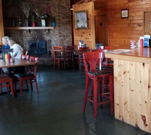Cozy restaurant interior with wooden decor, empty tables, and a couple dining in the background.