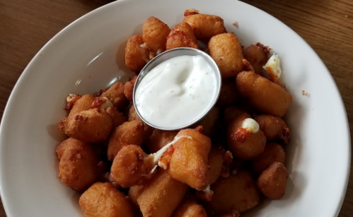 A bowl of golden-brown fried bites served with a small cup of creamy dipping sauce.