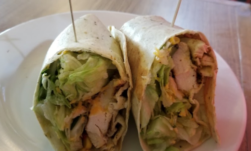 Two wrapped tortillas filled with lettuce, chicken, and cheese, secured with toothpicks, on a white plate.