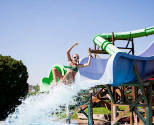 A woman in a green bikini slides down a colorful water slide, splashing into the pool below on a sunny day.