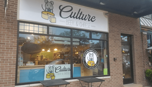 Exterior of "Culture Beer & Cheese" shop with a large window displaying the logo and inviting atmosphere.