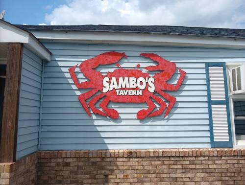 Sign for Sambo's Tavern featuring a large red crab on a blue building with a brick base.