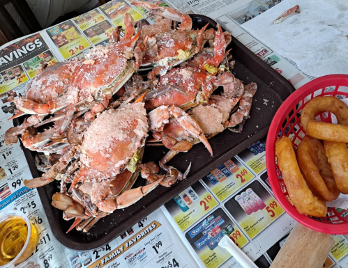 A tray of seasoned crabs with a side of fried dough on a table covered in newspaper ads.