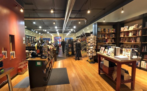 A cozy bookstore interior with wooden floors, shelves filled with books, and customers browsing. Warm lighting enhances the atmosphere.