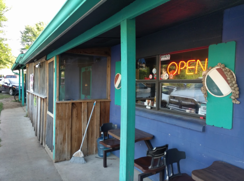A small, colorful building with an "OPEN" sign in the window and outdoor seating area.