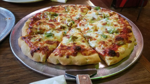 A freshly baked pizza with melted cheese and green peppers, sliced into eight pieces on a metal tray.