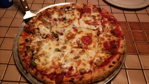 A large pizza topped with pepperoni, sausage, green peppers, and melted cheese on a round metal tray.