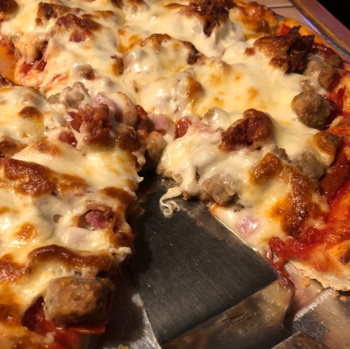 Close-up of a cheesy pizza topped with sausage and pepperoni, with a slice being lifted by a pizza cutter.