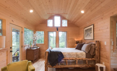Cozy wooden bedroom with large windows, a log bed, and rustic decor, surrounded by nature.