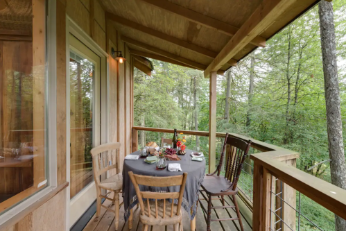 A cozy balcony with a table set for a meal, surrounded by lush greenery and wooden railings.