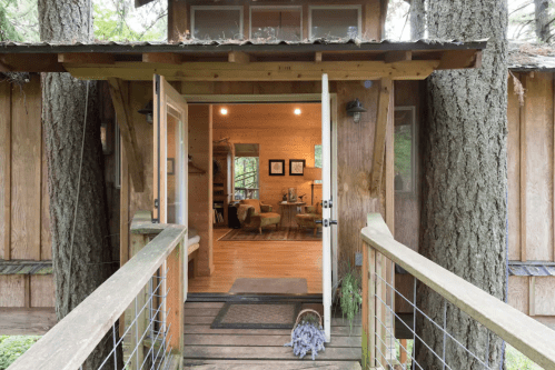 A rustic wooden entrance leads into a cozy, warmly lit interior with a view of a living space.