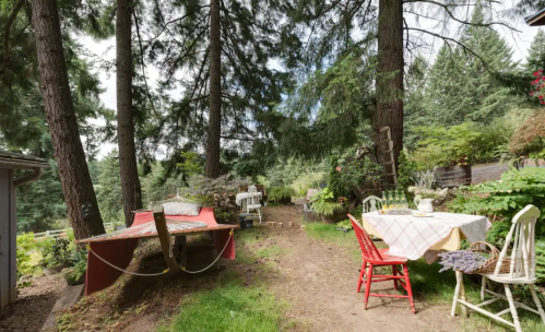 A serene garden path with a red table and chairs, surrounded by tall trees and lush greenery.
