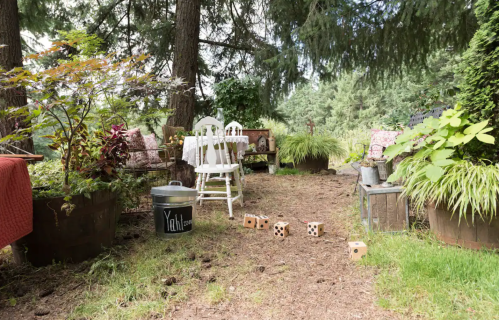 A serene garden path with chairs, a table, and decorative plants, featuring wooden dice scattered on the ground.