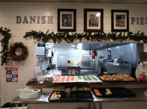 A cozy bakery display with holiday decorations, featuring trays of cookies and pies, and framed photos on the wall.