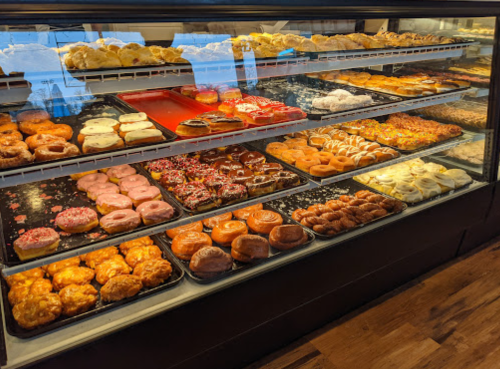A display case filled with a variety of colorful donuts and pastries, including glazed, frosted, and sprinkled options.