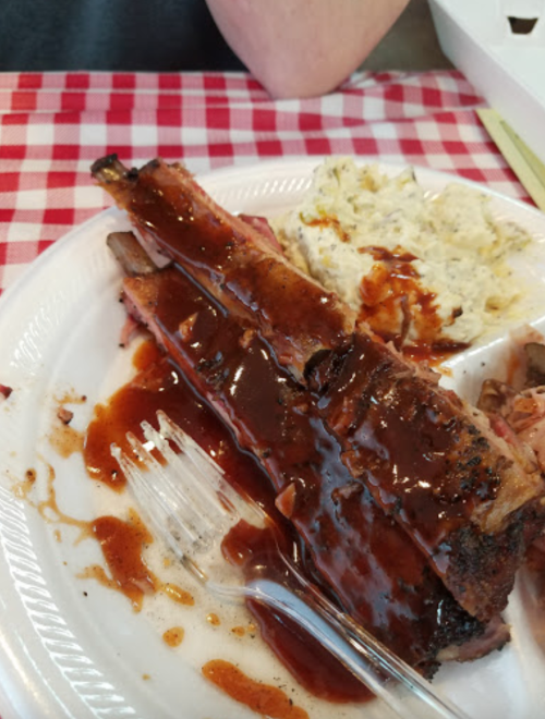 A plate of barbecue ribs covered in sauce, served with a side of creamy potato salad on a checkered tablecloth.