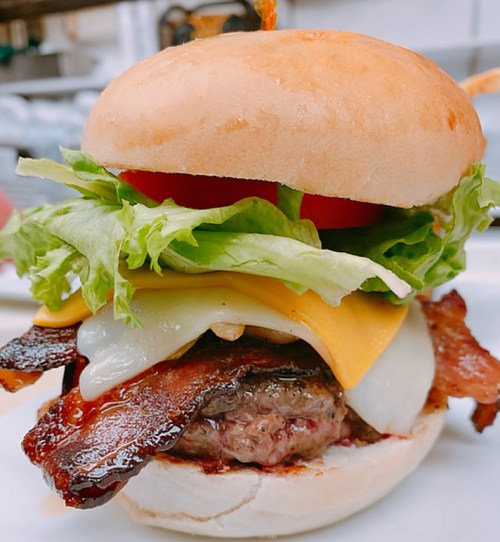 A juicy burger with bacon, lettuce, tomato, and melted cheese on a soft bun, served on a plate.