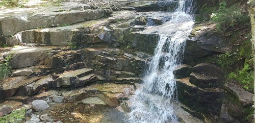 A serene waterfall cascading over rocky terrain, surrounded by lush greenery and natural beauty.