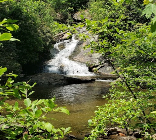 A serene waterfall cascades over rocks, surrounded by lush green foliage and a calm pool of water below.