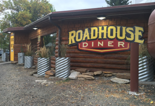 Exterior of a log cabin-style diner with a large "Roadhouse Diner" sign and decorative planters.
