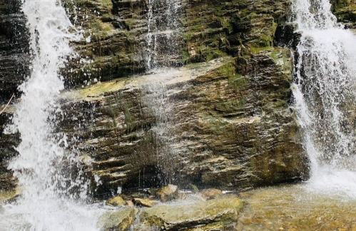 A cascading waterfall flows over rocky terrain, creating a serene natural scene with splashes of water.