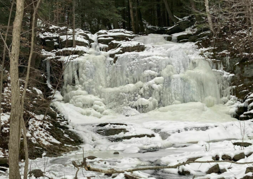 A frozen waterfall surrounded by snow-covered rocks and trees in a winter landscape.