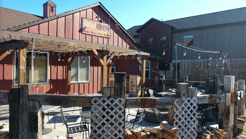 Outdoor seating area of a rustic building with a sign for a brew pub, surrounded by wooden fences and string lights.