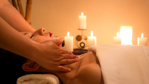 A person receiving a facial massage in a serene spa setting, surrounded by glowing candles.