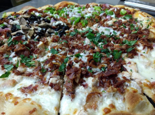 A close-up of a pizza topped with various ingredients, including herbs, meats, olives, and vegetables.