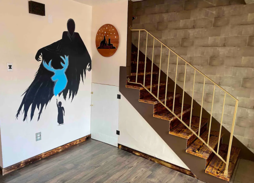 A staircase in a room with a dark mural of a figure and a blue deer on the wall, and a circular wooden decoration.