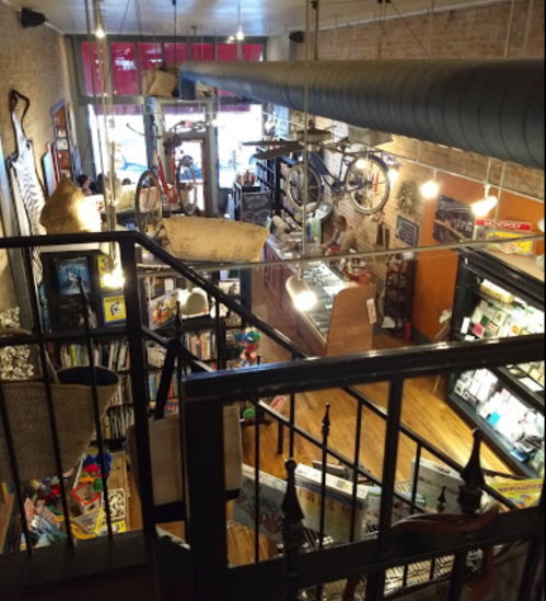 A cozy, eclectic shop interior with bikes hanging from the ceiling and various items displayed on shelves.