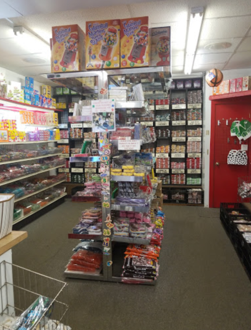 A colorful candy store aisle with shelves filled with various sweets and snacks, including a display stand in the center.
