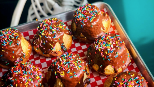 A tray of chocolate-covered muffins topped with colorful sprinkles on a red checkered paper.