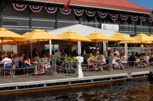 A lively waterfront restaurant with yellow umbrellas, people dining, and festive decorations along the building.