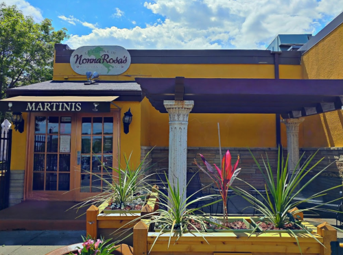 Exterior of Noma Rosa's restaurant featuring a sign, plants, and a welcoming entrance with a martini theme.