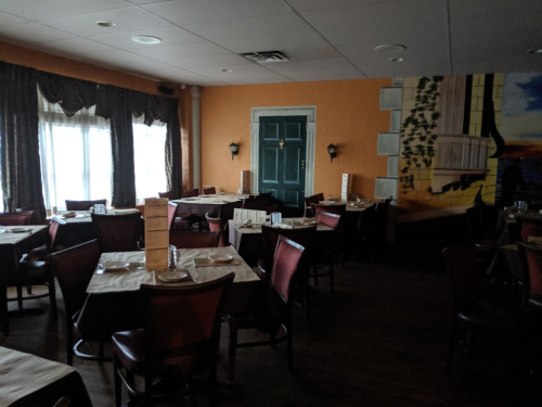 A dimly lit restaurant with empty tables, dark red chairs, and an orange wall featuring a mural.