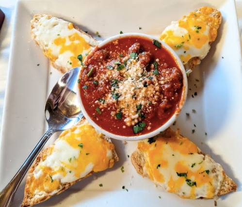 A plate with cheesy bread slices arranged around a bowl of marinara sauce, topped with herbs and cheese.