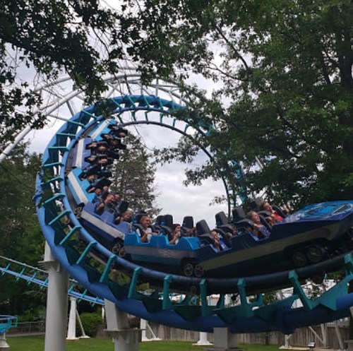 A roller coaster twists through a loop with excited riders enjoying the thrill on a cloudy day.