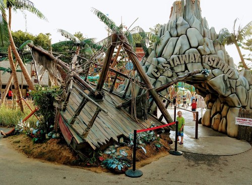 A child stands near a shipwreck entrance to Castaway Island, surrounded by tropical plants and a playful atmosphere.
