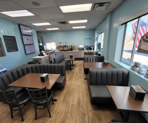 A cozy diner interior with booths and tables, featuring a counter and drink station, and large windows with an American flag.