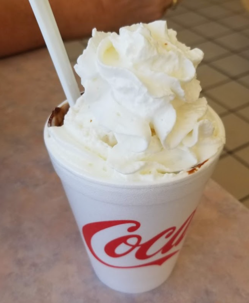 A white cup with a Coca-Cola logo filled with a dessert topped with whipped cream.
