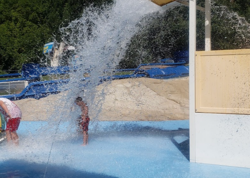 Two children play in a water park, with a large splash of water cascading from a structure above them.
