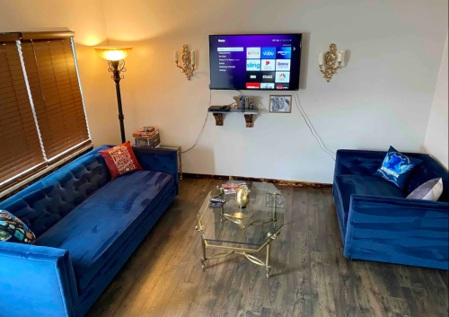 A cozy living room with blue sofas, a glass coffee table, and a wall-mounted TV displaying streaming options.
